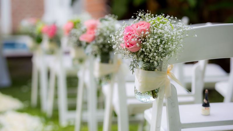 Tarros con rosa y paniculata en los respaldos de las sillas
